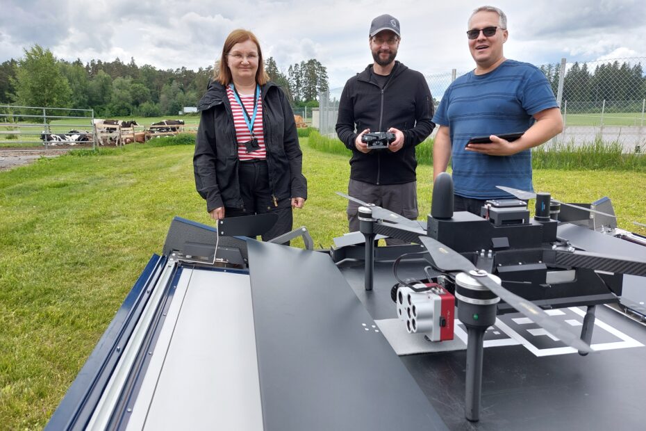 Eija Honkavaara, Teemu Hakala and Juha Suomalainen in countryside landscape in fron of Drone-in-a-box.