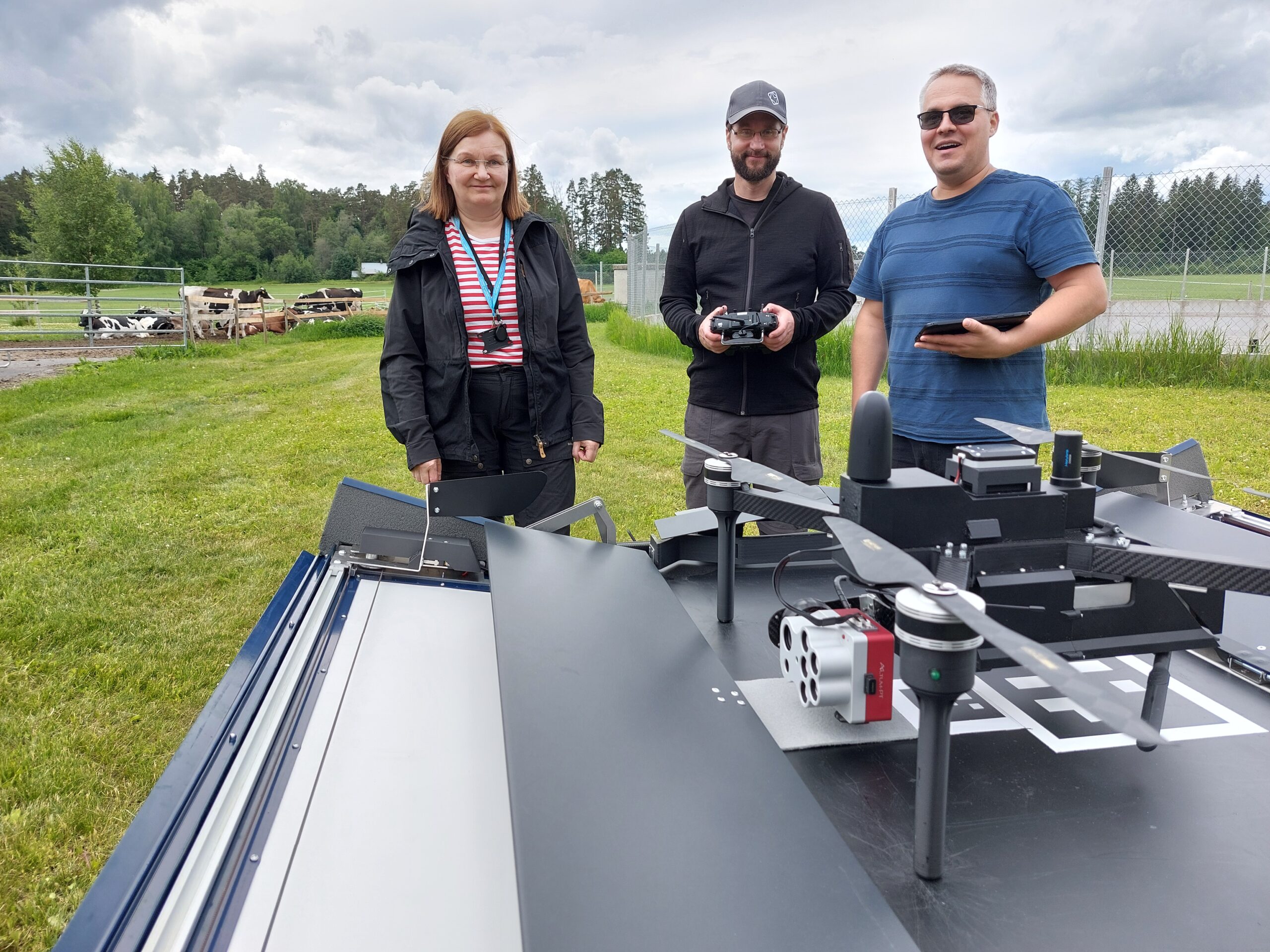 Eija Honkavaara, Teemu Hakala and Juha Suomalainen in countryside landscape in fron of Drone-in-a-box.